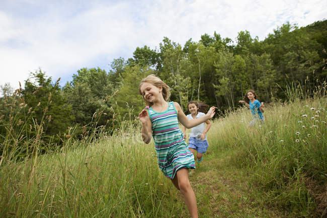 Três meninas rindo e correndo através de grama verde . — Fotografia de Stock
