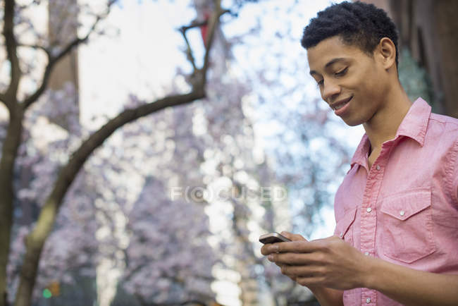 Young man in park in spring using mobile phone. — Stock Photo