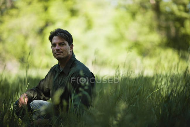 Человек сидит на траве в саду и смотрит в камеру . — стоковое фото