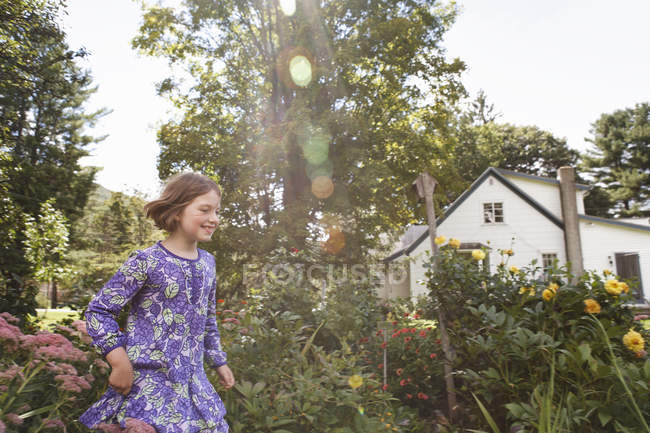Child in patterned blue dress running through house garden. — Stock Photo