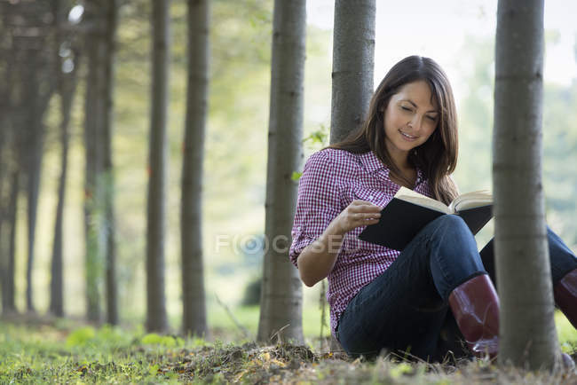 Femme assise et lisant un livre sous les arbres dans les bois
. — Photo de stock