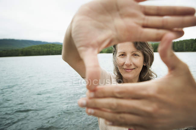 Mulher olhando através das mãos, enquanto em pé na frente do lago país — Fotografia de Stock