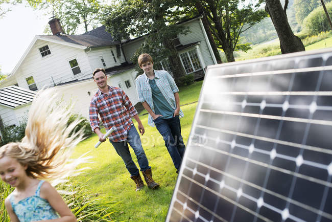 Mid adult man with son and daughter walking by solar panel in farmhouse garden. — Stock Photo