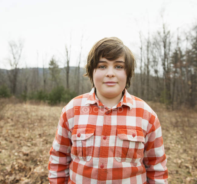 Мальчик в красной клетчатой рубашке стоит в осеннем лесу . — стоковое фото