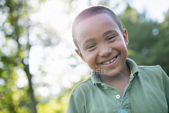 Elementary age boy looking in camera outdoors in sunny park. — Stock Photo