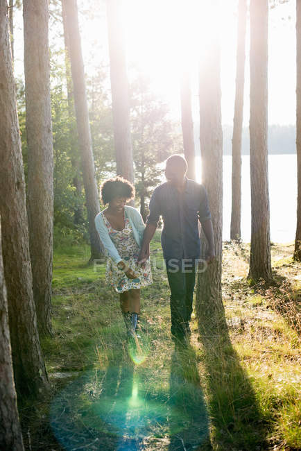 Pareja joven caminando en el bosque por la orilla del lago . - foto de stock