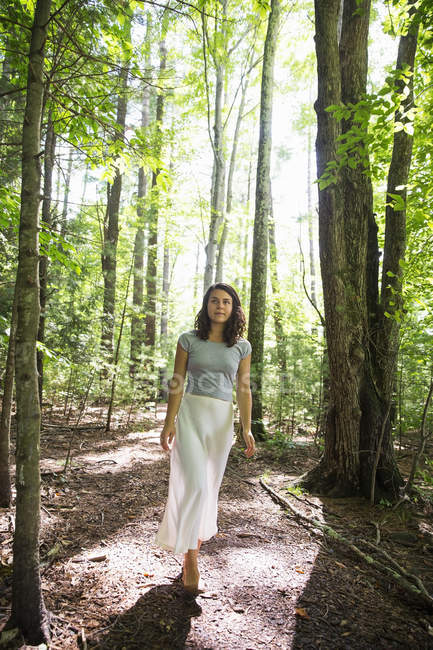 Young woman in long skirt walking through sunny woodland. — Stock Photo