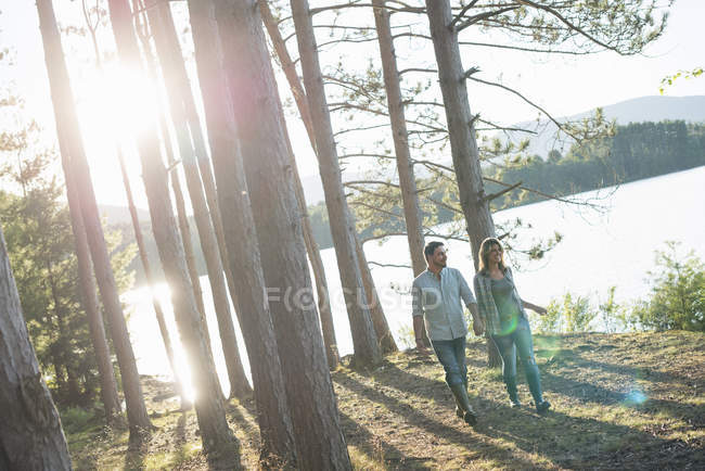 Couple walking hand in hand in woodland on shore of forest lake. — Stock Photo