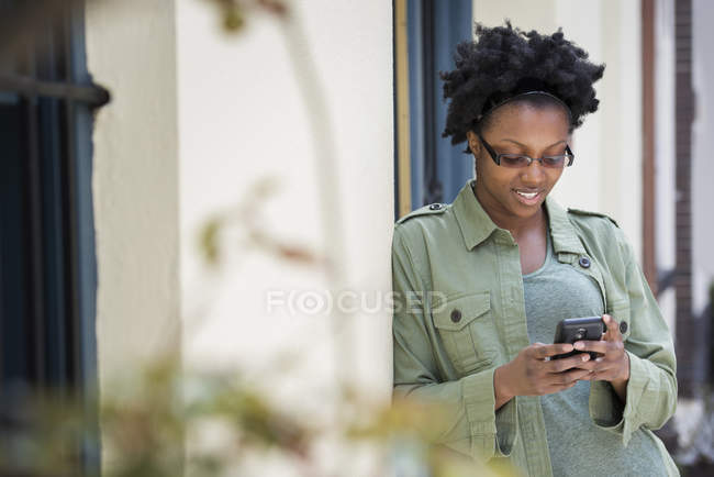 Woman leaning against door and checking phone. — Stock Photo