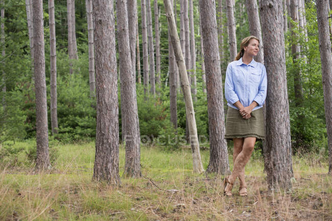 Mature woman standing and leaning on tree in woodland. — Stock Photo