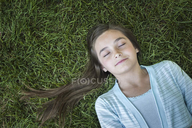 Visão aérea da menina com o cabelo longo ventilado deitado na grama verde com os olhos fechados . — Fotografia de Stock