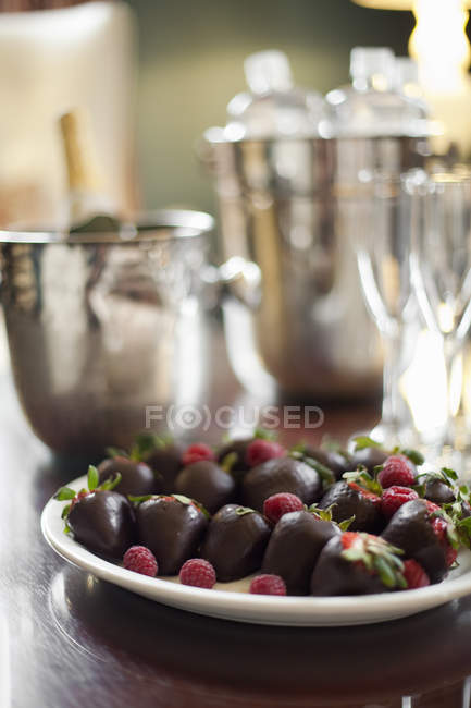Prato de morangos orgânicos em chocolate com framboesas, champanhe e copos . — Fotografia de Stock
