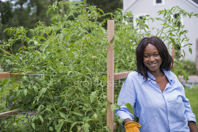 Woman leaning on fence and smiling in vegetable garden. — Stock Photo