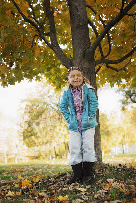 Elementary age girl standing under autumnal tree on farm. — Stock Photo