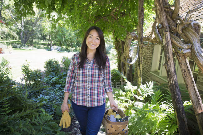 Junge Frau mit Schutzhandschuhen und Korb mit Werkzeug auf Biobauernhof. — Stockfoto