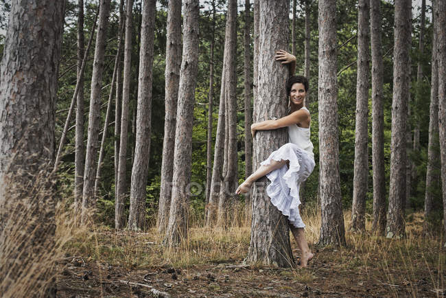 Жінка обіймає дерево під час танцю і дивиться в камеру в лісі . — стокове фото