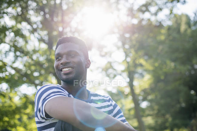 Young man in striped shirt under shade of trees in woodland. — Stock Photo