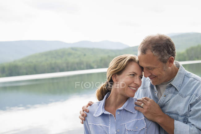 Mature couple standing face to face by lake shore. — Stock Photo