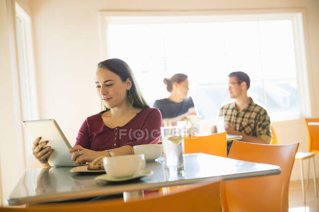 Жінка в кав'ярні читає з планшетним комп'ютером з людьми, які розмовляють на задньому плані . — стокове фото