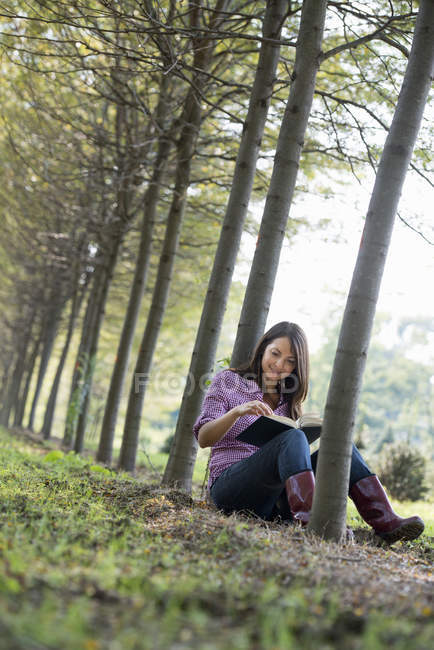 Frau sitzt und liest Buch unter Bäumen im Wald. — Stockfoto
