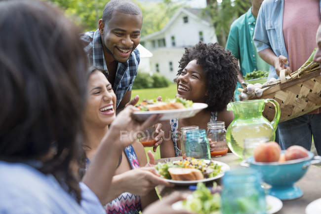 Молоді друзі діляться тарілками з їжею за столом для пікніка в сільському саду . — стокове фото