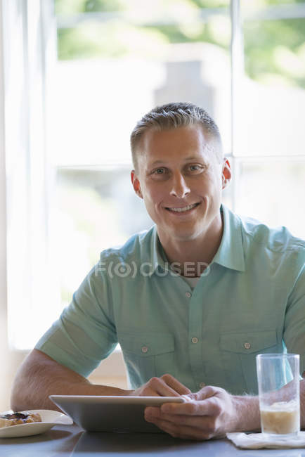 Mann mit kurzen Haaren sitzt am Cafétisch und hält digitales Tablet in der Hand. — Stockfoto