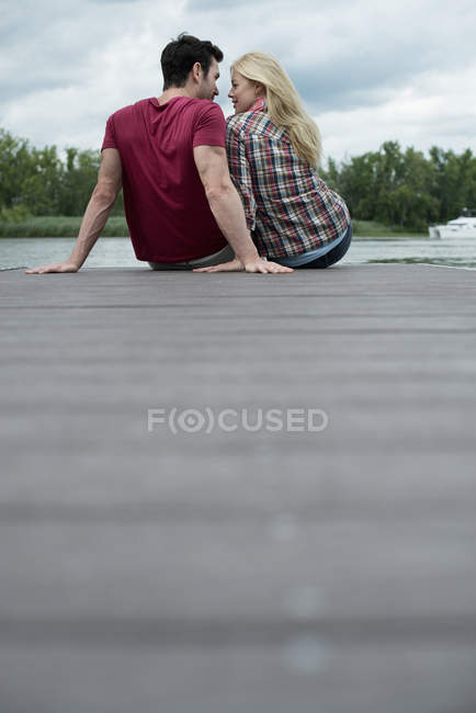 Homem e mulher sentados juntos no molhe pelo lago . — Fotografia de Stock