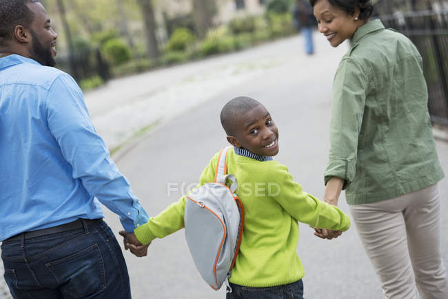 Ragazzo con lo zaino guardando oltre la spalla mentre cammina con i genitori per strada . — Foto stock