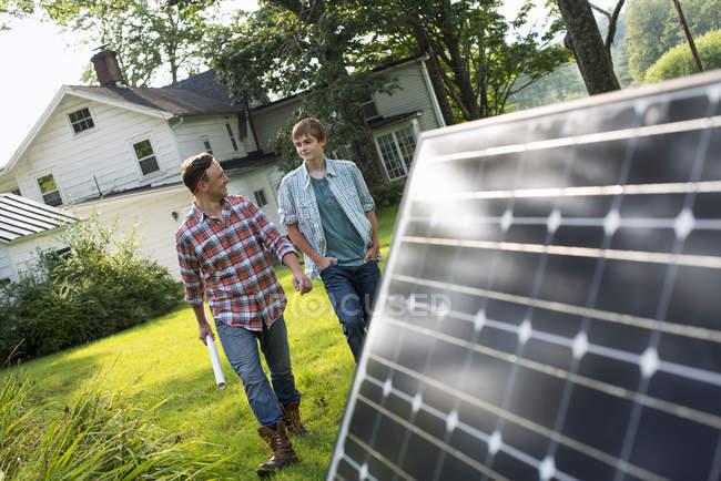 Mid adult man with son walking by solar panel in farmhouse garden. — Stock Photo
