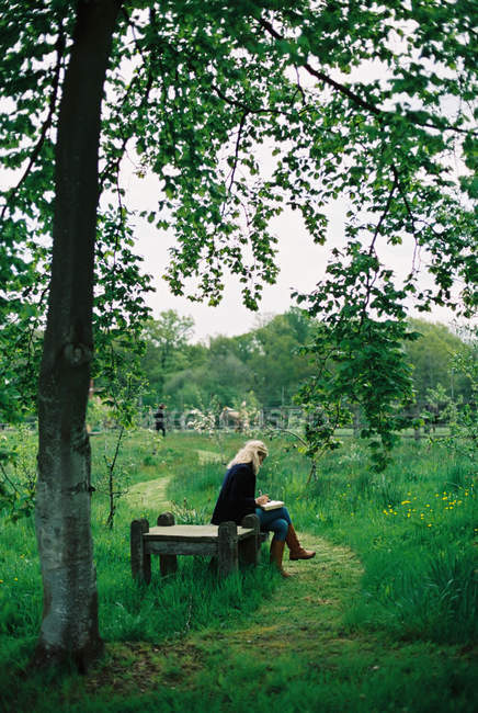 Жінка сидить на дерев'яному сидінні в зеленій сільській місцевості . — стокове фото