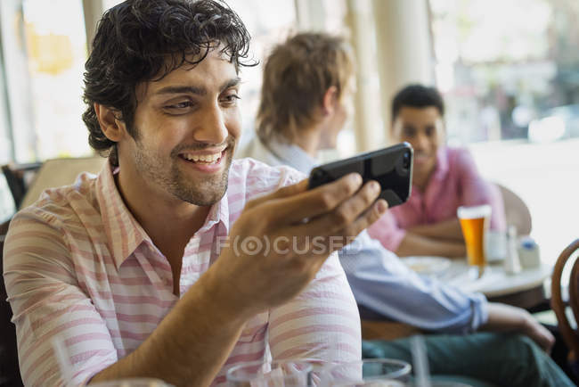 Young man using smartphone in cafe with people in background. — Stock Photo