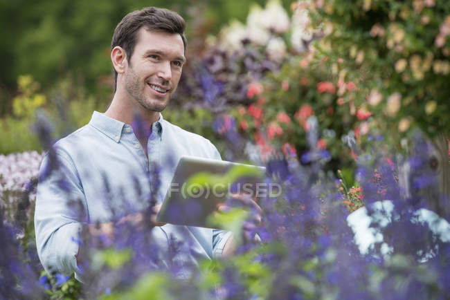Hombre adulto medio usando tableta digital en vivero de plantas orgánicas . - foto de stock
