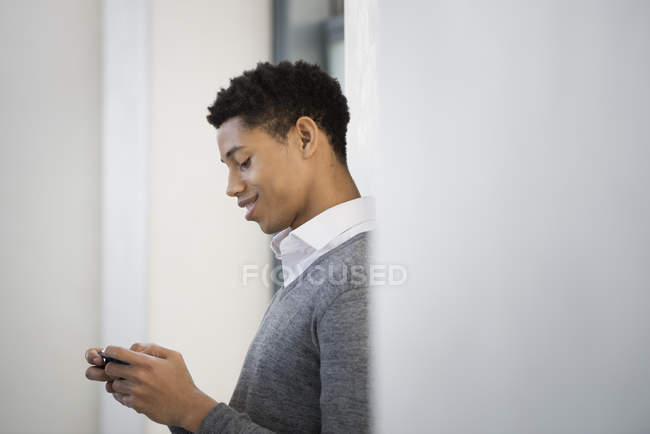Junger Mann im grauen Pullover nutzt Smartphone im Haus. — Stockfoto