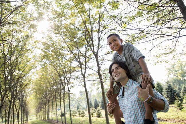 Low angle view of young man giving boy piggyback in woods. — Stock Photo