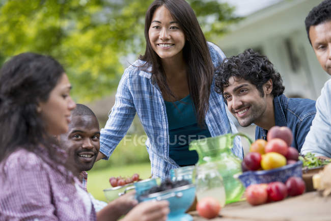 Amigos sentados à mesa ao ar livre no jardim com frutas e legumes . — Fotografia de Stock