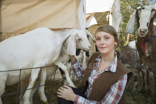 Woman posing with goats in pen leaning over fence at farm. — Stock Photo