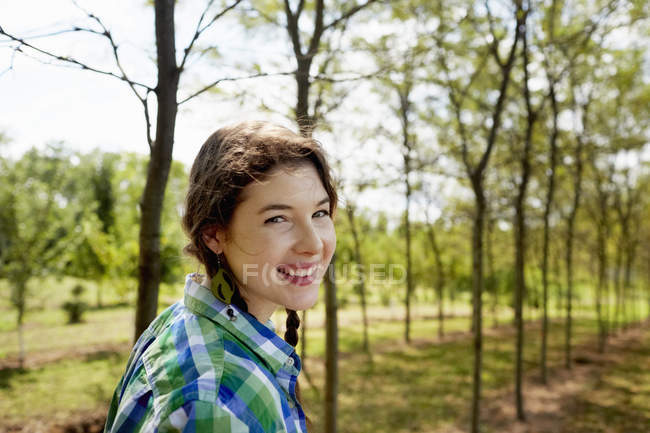 Jovem de camisa verde verificada com tranças olhando na câmera no campo . — Fotografia de Stock