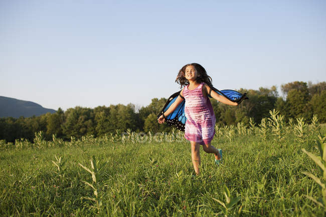 Pre-adolescent girl running across field wearing fabric butterfly wings. — Stock Photo