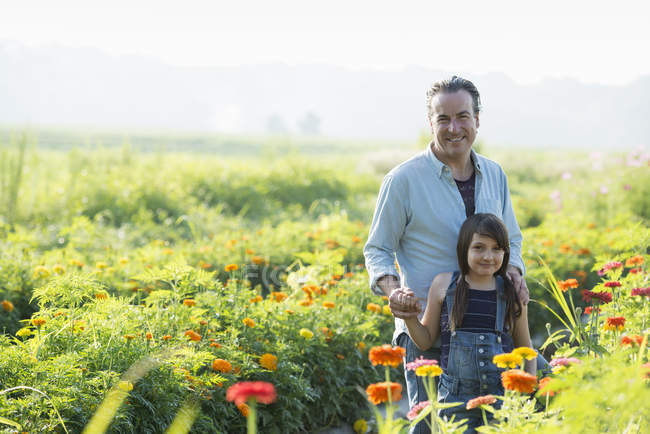 Mature man with daughter posing in green field of flowers. — Stock Photo