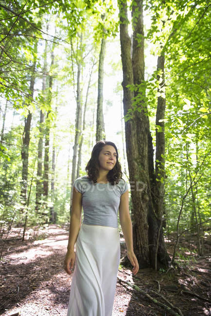 Junge Frau im langen Rock spaziert durch sonnigen Wald. — Stockfoto