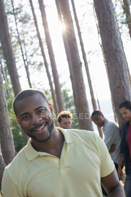 Hombre adulto sonriendo y mirando en cámara con amigos reunidos en pinos a orillas del lago
. - foto de stock