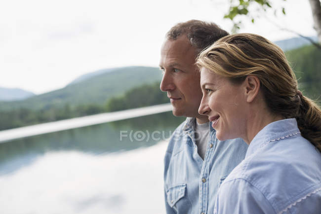 Mature couple standing by lake shore and looking at view. — Stock Photo