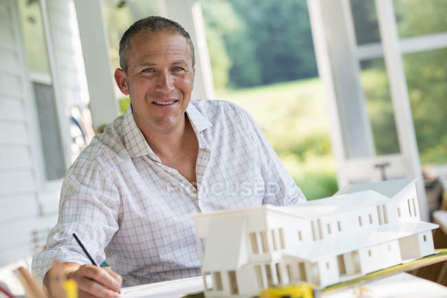 Mature man working on model of farmhouse at table in countryside. — Stock Photo