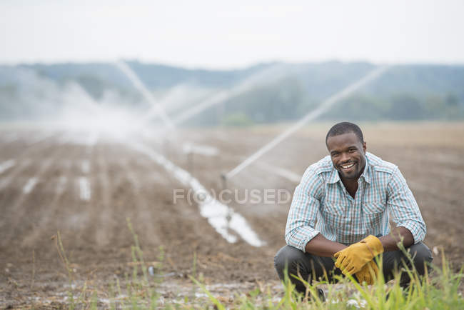 Молоді чоловіки фермер в робочий одяг на органічні поля з Зрошувальні води спринклери. — стокове фото
