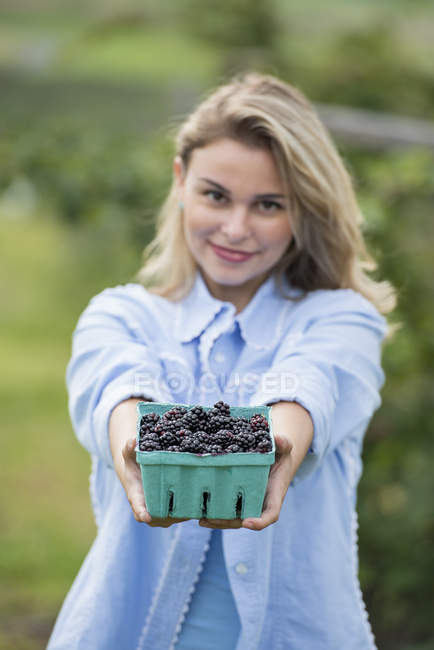 Young woman holding full punnet of glossy berries. — Stock Photo