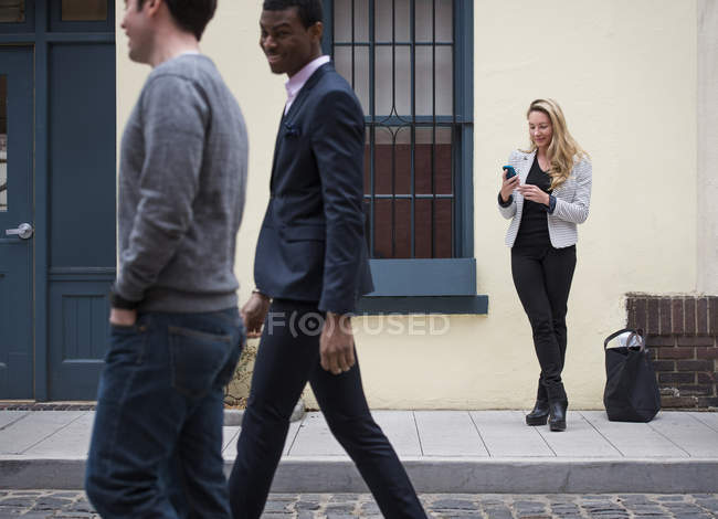 Woman using smartphone with two men walking past on cobbled street. — Stock Photo