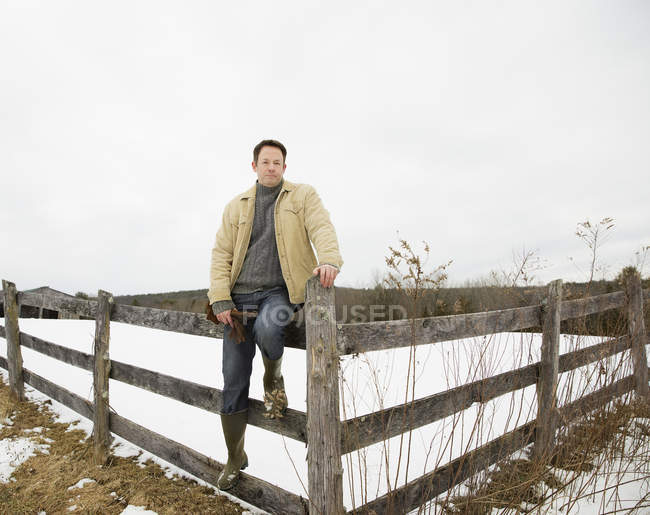 Mature man posing on fence  in countryside. — Stock Photo