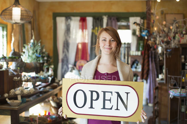 Woman standing in antique store and holding OPEN sign. — Stock Photo