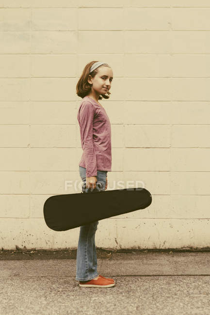Chica pre-adolescente llevando estuche de violín en la calle urbana . - foto de stock
