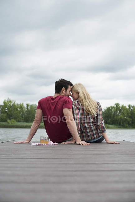Man and woman sitting together on jetty by lake. — Stock Photo